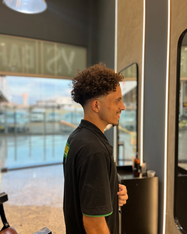 Homem com cabelo penteado para trás e barba bem aparada.